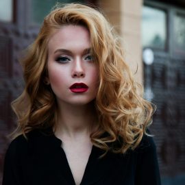 Elegant portrait of a woman in a black top with striking red lips and flowing blond hair.
